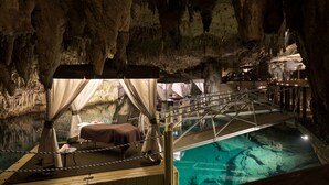 Habitación de hotel con temática de cueva, con cama, una mesita y vista a una piscina.