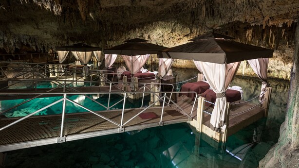 Un hotel cueva con piscina, camas con dosel y un puente metálico sobre el agua.