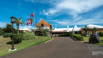 A hotel entrance with a clear driveway, palm trees, and flags.