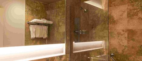 Un baño moderno con ducha envuelta en vidrio, un espejo grande y un tocador con lavamanos y perchero.