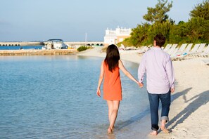 A couple walking on a sandy beach with a clear sky and calm sea.