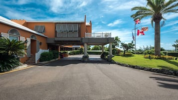 Ein Hotel mit Eingangsbereich, überdachtem Gang, Palmen und Flaggen.