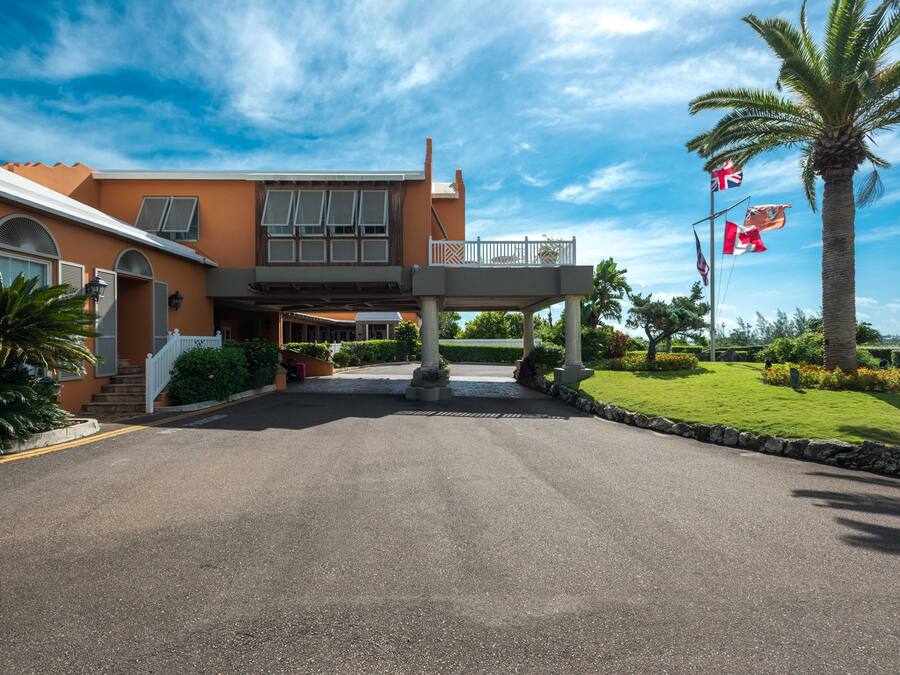 Ein Hotel mit Eingangsbereich, überdachtem Gang, Palmen und Flaggen.