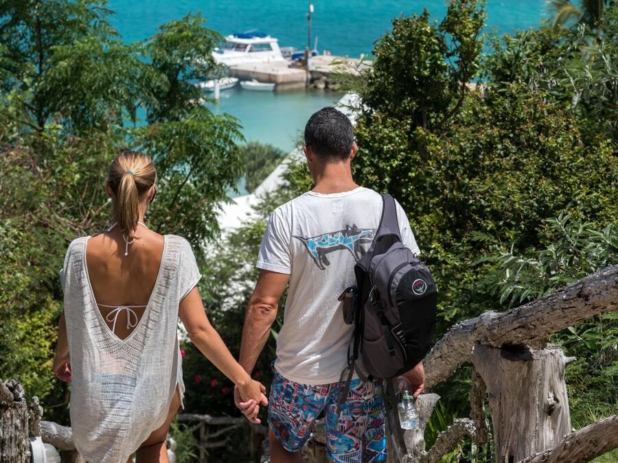 Una pareja camina por un sendero de piedra hacia una masa de agua con barcos al fondo.
