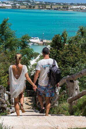 Una pareja camina por un sendero de piedra hacia una masa de agua con barcos al fondo.