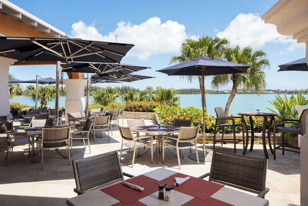 An outdoor patio area with tables and chairs, umbrellas, and a view of a lake.