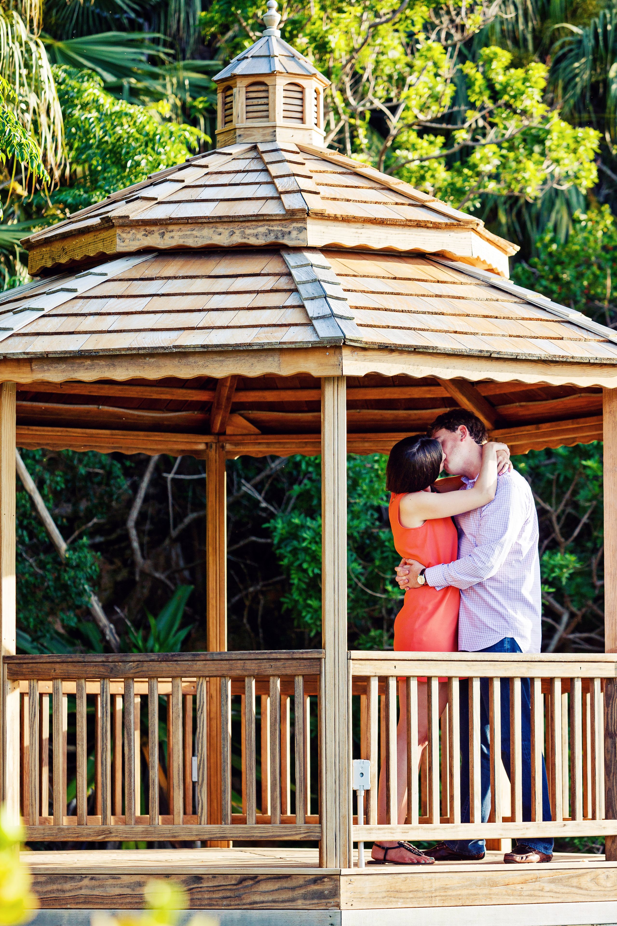 A gazebo with a wooden roof and a small tower, surrounded by lush greenery.