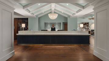 A reception area with a central counter, a person standing behind it, and a modern chandelier.