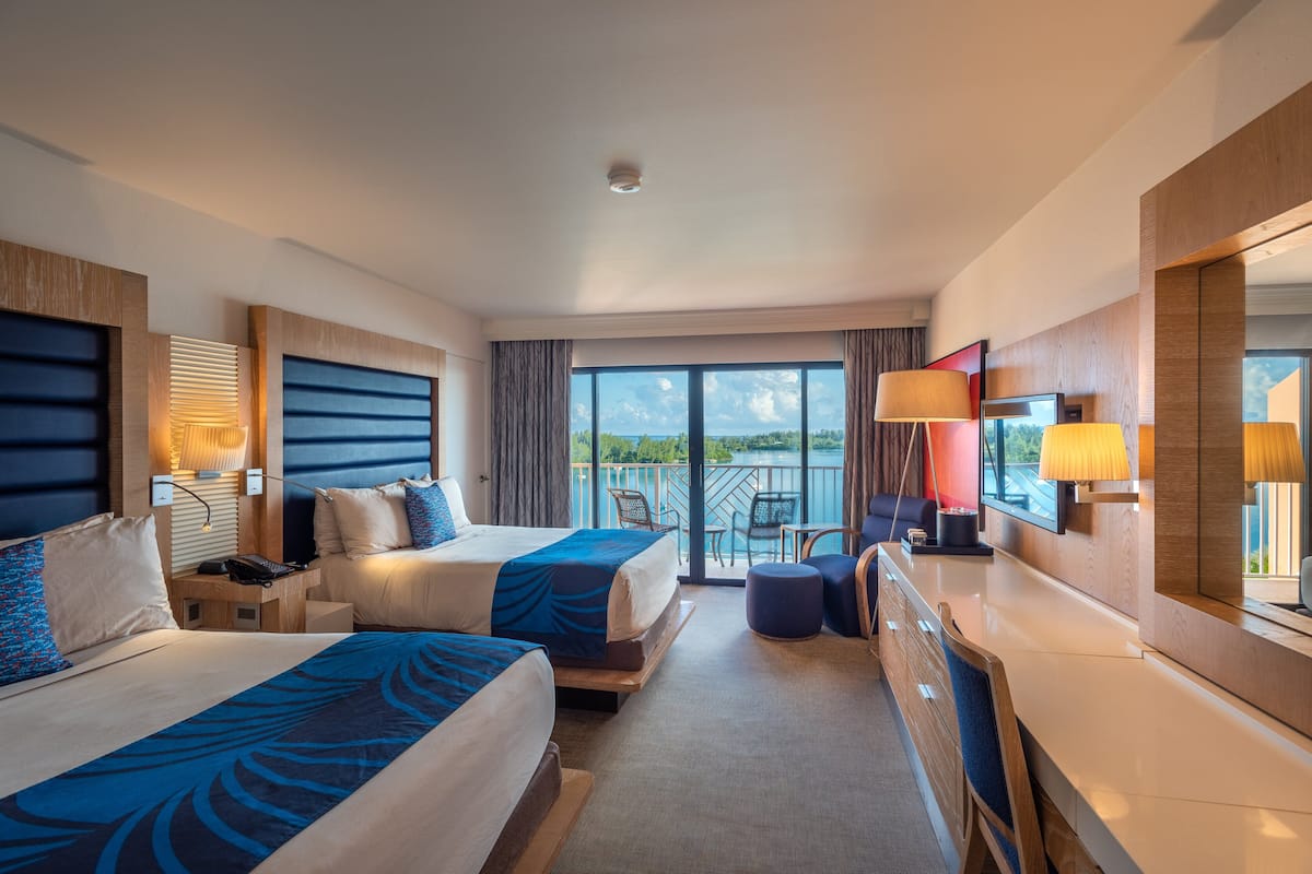 A hotel room with two beds, a balcony, and a view of the sea.