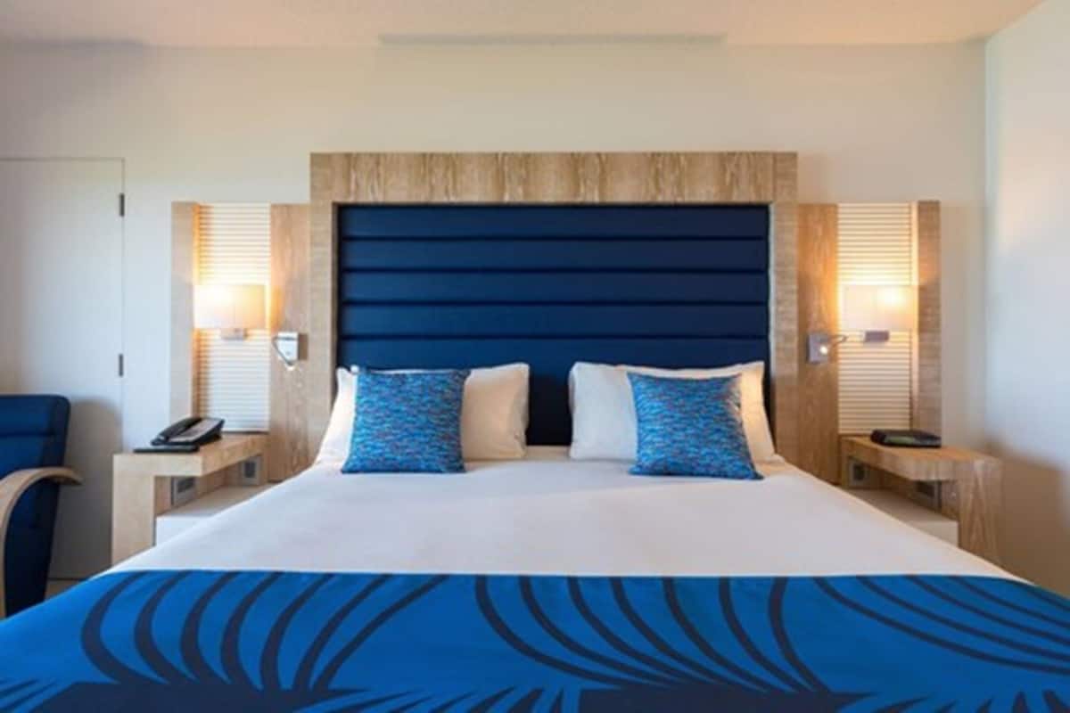 A hotel room with a large bed, two bedside tables, a chair, and a wooden headboard.