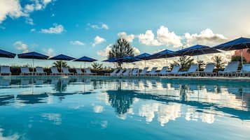 Relax by the pool surrounded by lush trees and comfortable lounge chairs under shaded umbrellas.