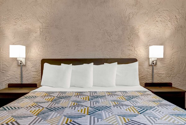 A hotel room with a bed, two bedside tables, and two wall-mounted lamps.