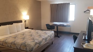 A hotel room with a bed, desk, chair, television, and telephone.