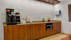 A kitchen with a wooden countertop, a coffee machine, a microwave, and a potted plant.