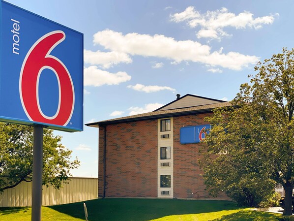 A motel sign with the number 6, a brick building with a flat roof, and a tree in the foreground. - Motel 6 Elk Grove Village, IL - O'Hare (Elk Grove Village)