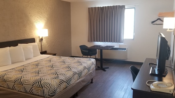 A hotel room with a large bed, a desk, a chair, a television, and a telephone.
