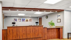 A reception area with a wooden counter, framed pictures on the wall, a clock, and a potted plant.