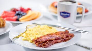 Un plato de desayuno con huevos revueltos y tocino, una taza de café y un plato de fruta.