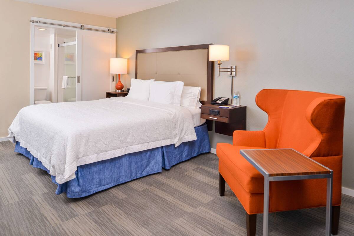 A hotel room with a bed, a nightstand, a chair, and a small table.