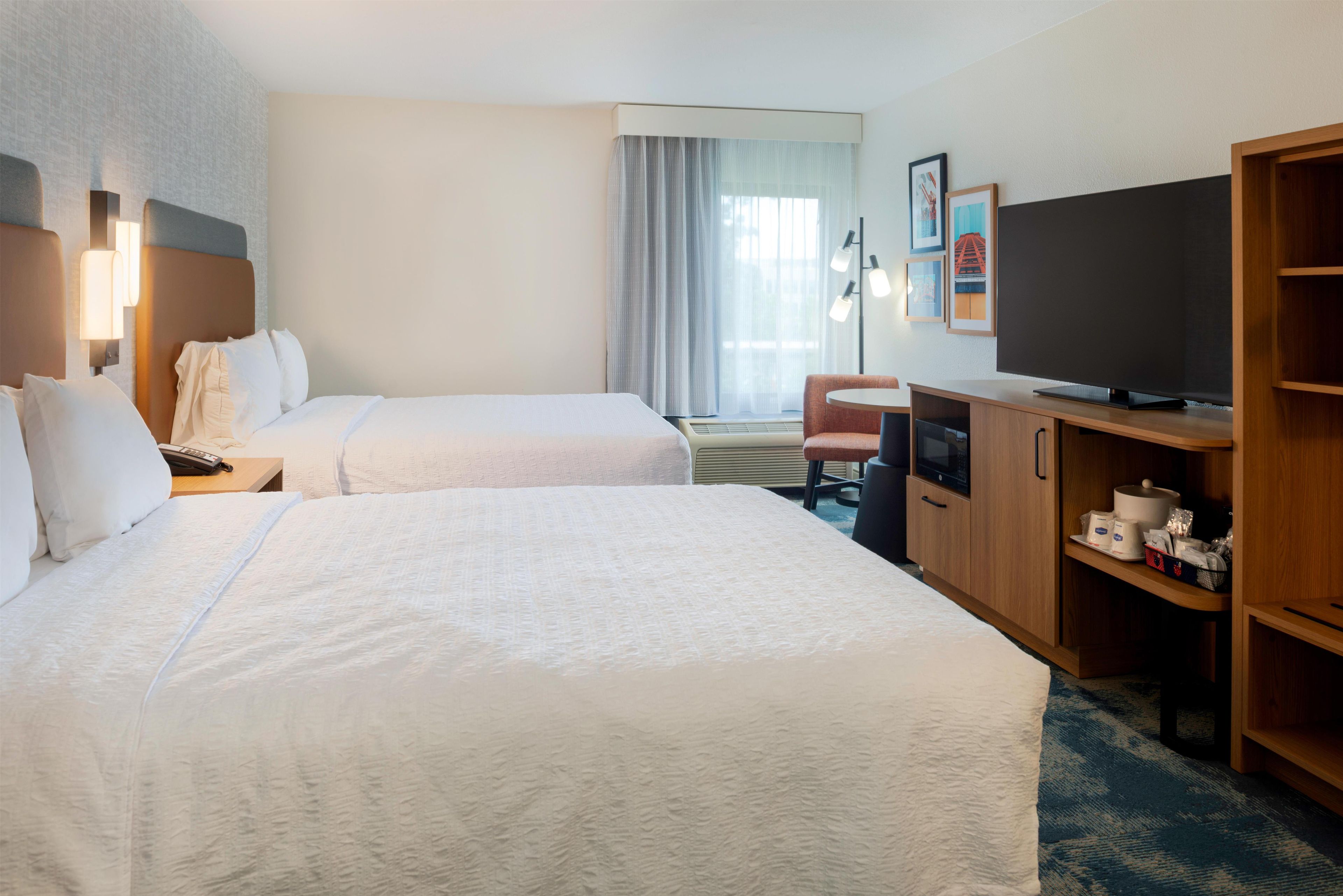 A hotel room with two beds, a television, a desk, and a chair.
