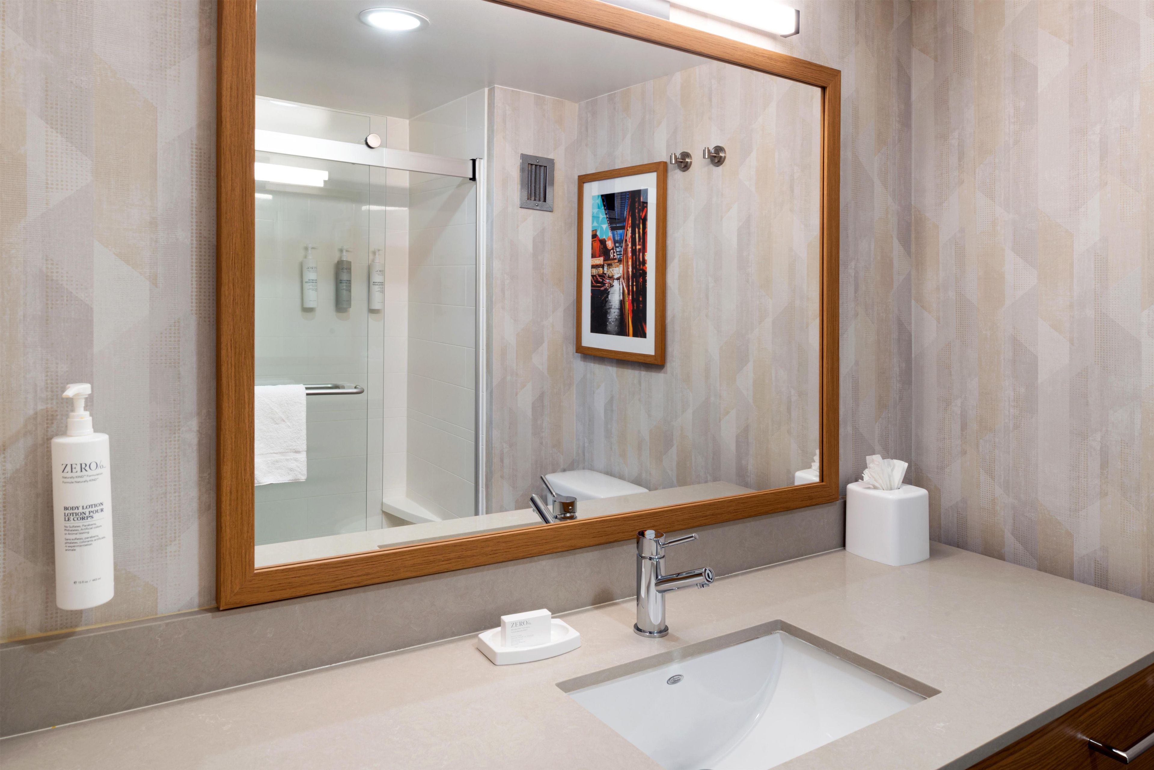 Un baño con un espejo grande, un lavabo, un perchero para toallas y un cuadro en la pared.