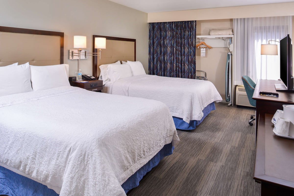 A hotel room with two beds, a desk, a chair, a TV, and a bathroom area.