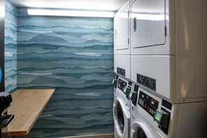 A laundry room with a wall-mounted washing machine and dryer, a wooden bench, and a patterned wall.