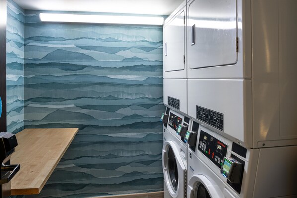 A laundry room with a wall-mounted washing machine and dryer, a wooden bench, and a patterned wall.