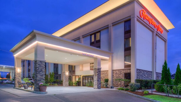 Um hotel Hampton Inn com entrada coberta, pilares de pedra e fachada bem iluminada.
