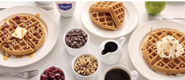 A table with waffles, chocolate chips, and syrup.
