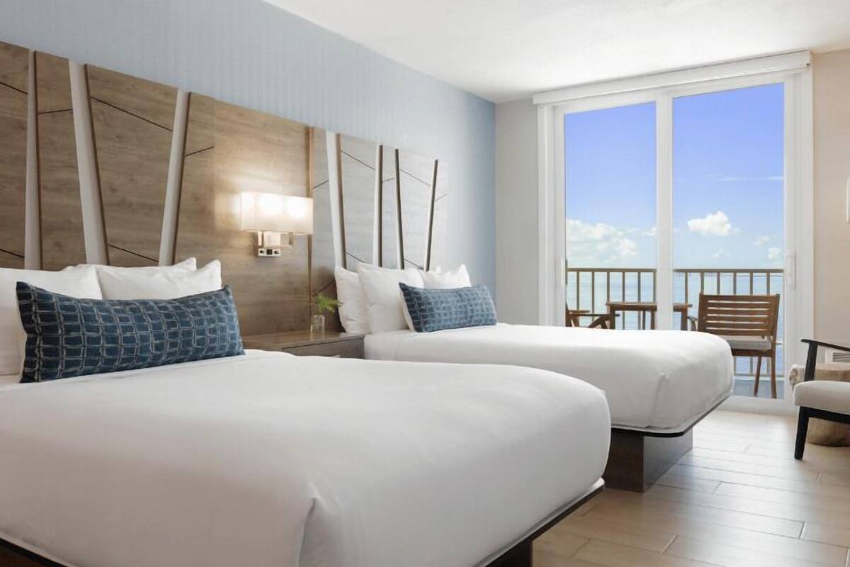 Een hotelkamer met twee bedden, een balkon en een zitgedeelte met uitzicht.