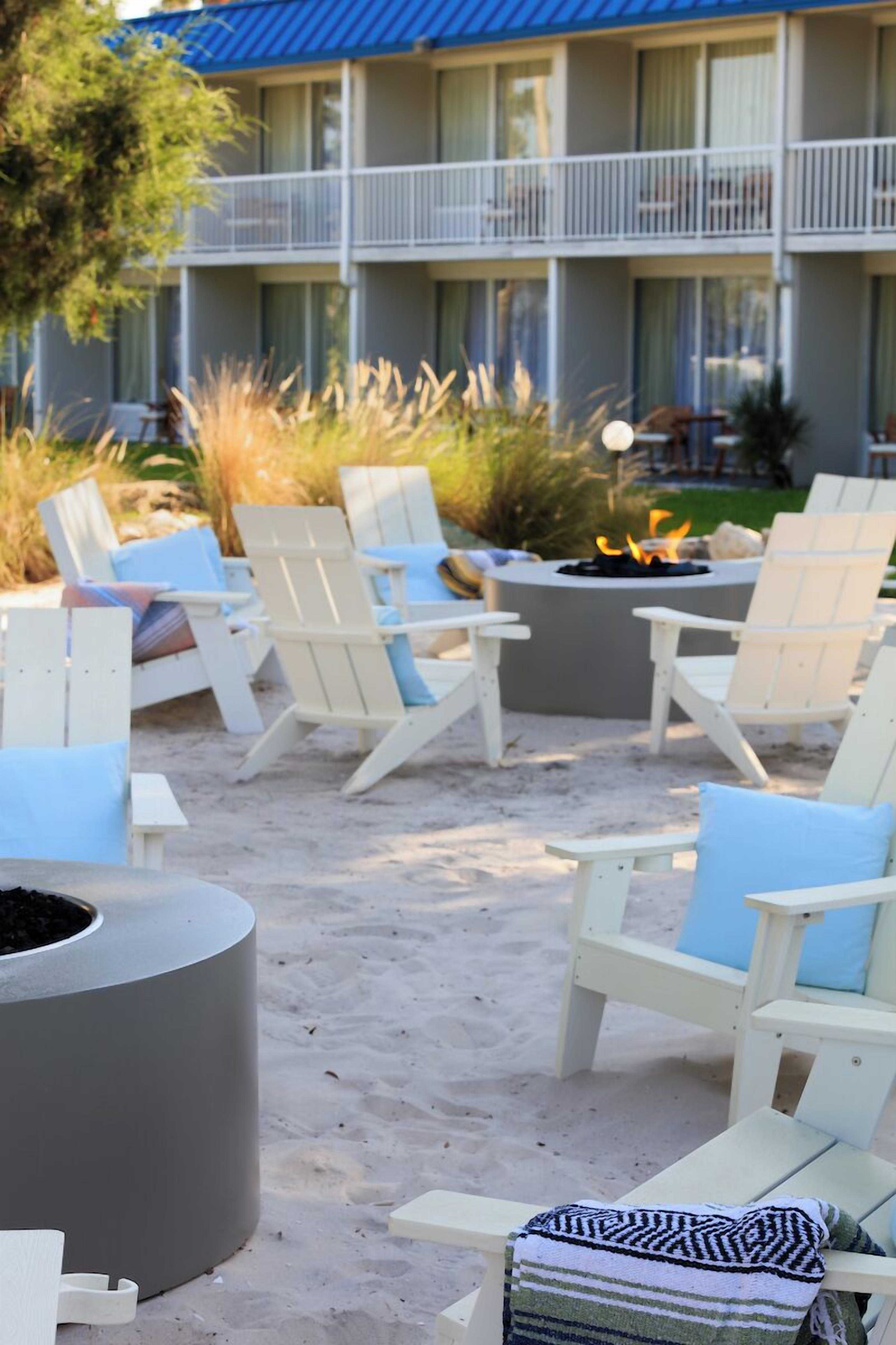 Area relax in spiaggia con poltroncine Adirondack bianche, un braciere e un vaso da fiori grande.