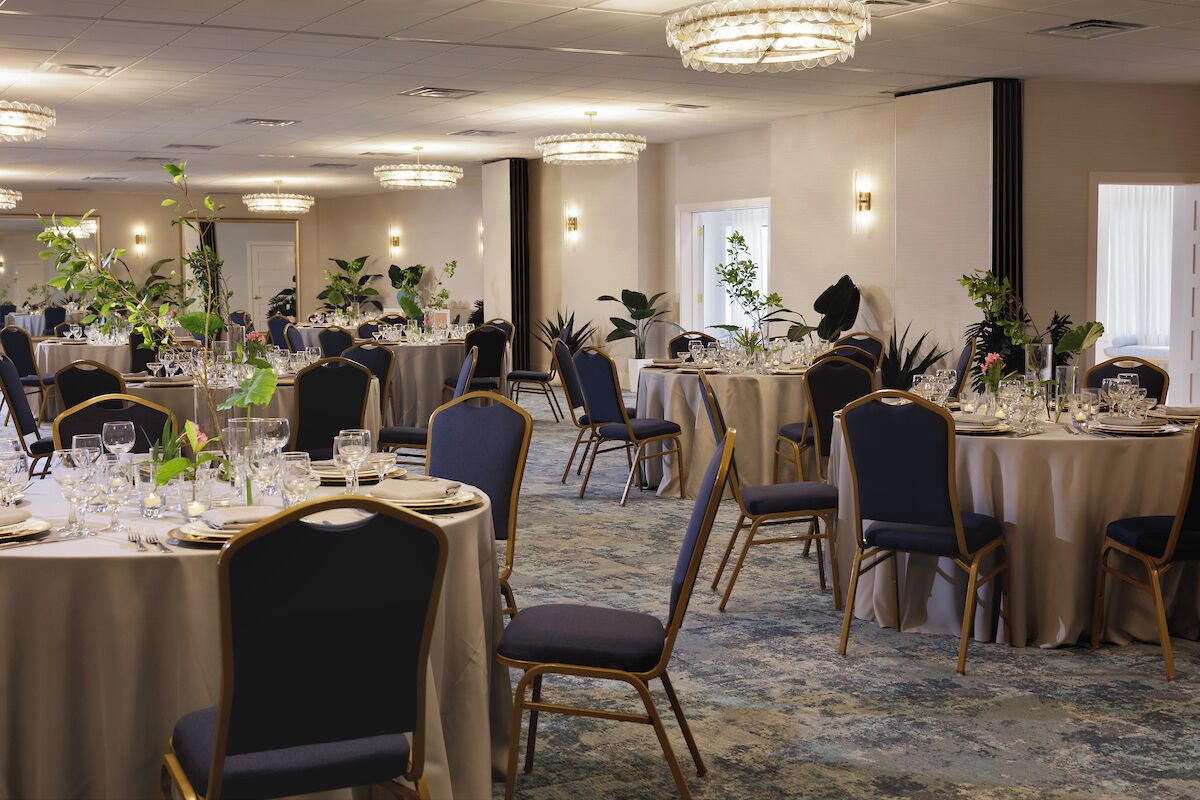 A banquet hall with round tables, chairs, and chandeliers.
