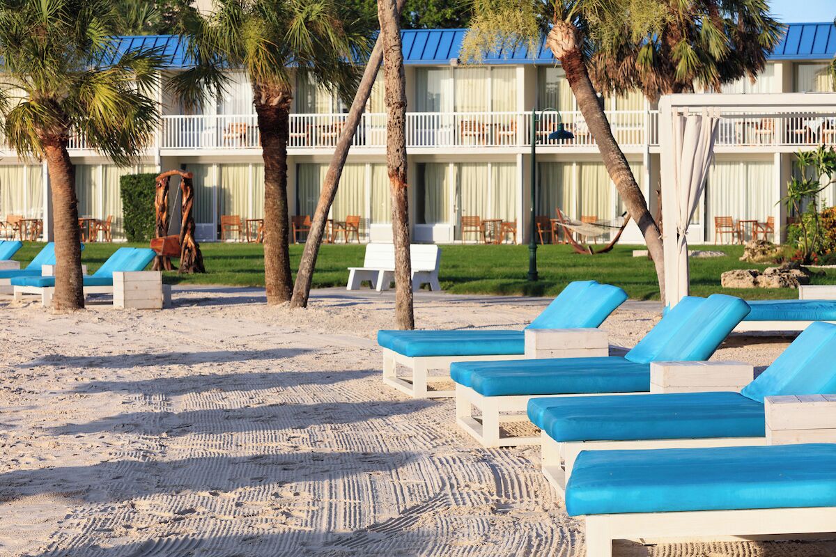 A beachside hotel with lounge chairs, palm trees, and a building with balconies.