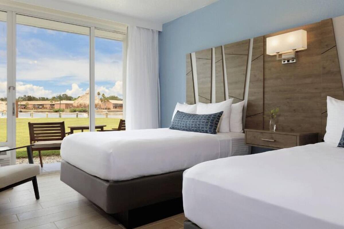 Een hotelkamer met twee bedden, een groot raam met uitzicht op een golfbaan en een houten hoofdeinde.