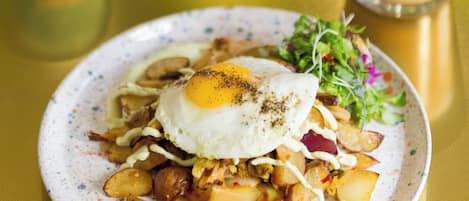 Un plato de desayuno con huevos, papas y vegetales verdes, un vaso de café helado y un batido verde sobre una mesa amarilla.