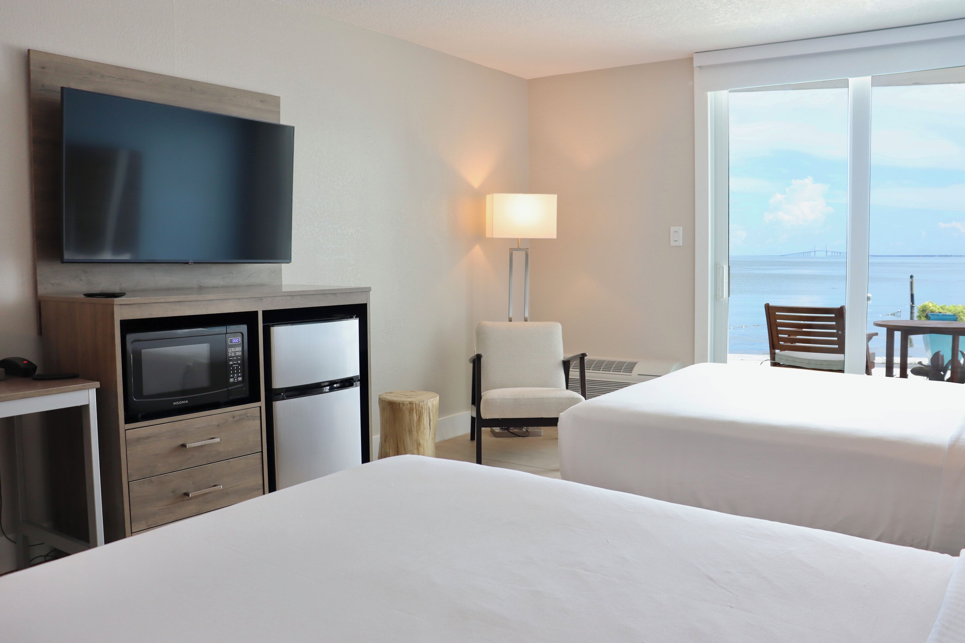 Habitación de hotel con dos camas, televisor, microondas, lámpara y vista al mar.