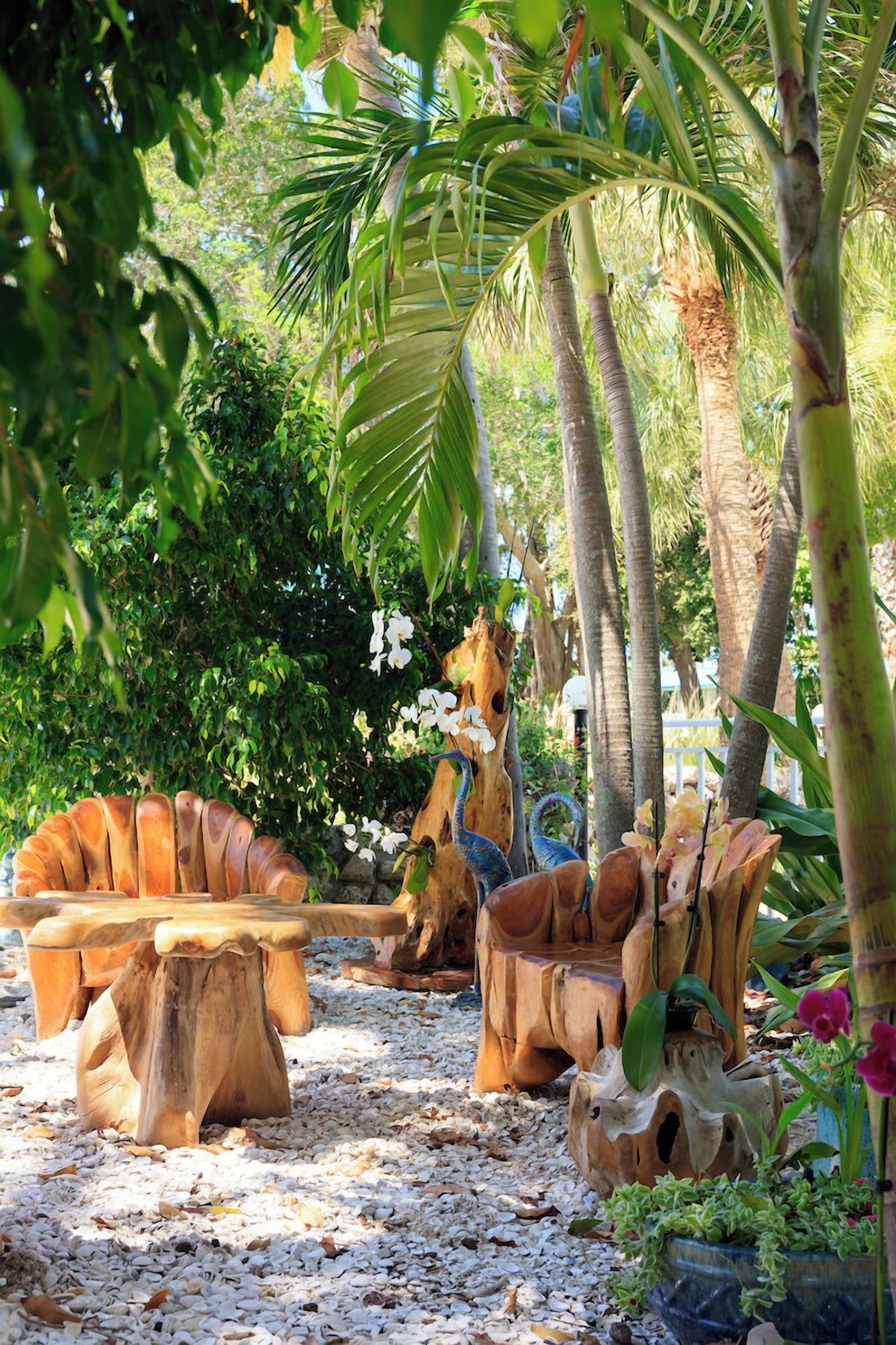 Un jardín tropical con mobiliario de madera y una escultura de pájaro.
