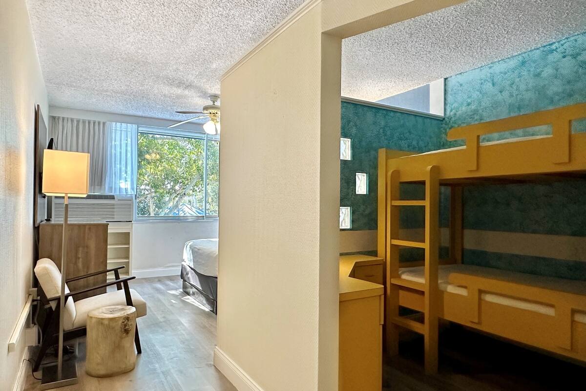 Een kamer met een stapelbed, een bureau, een stoel, een lamp en een raam met gordijnen.