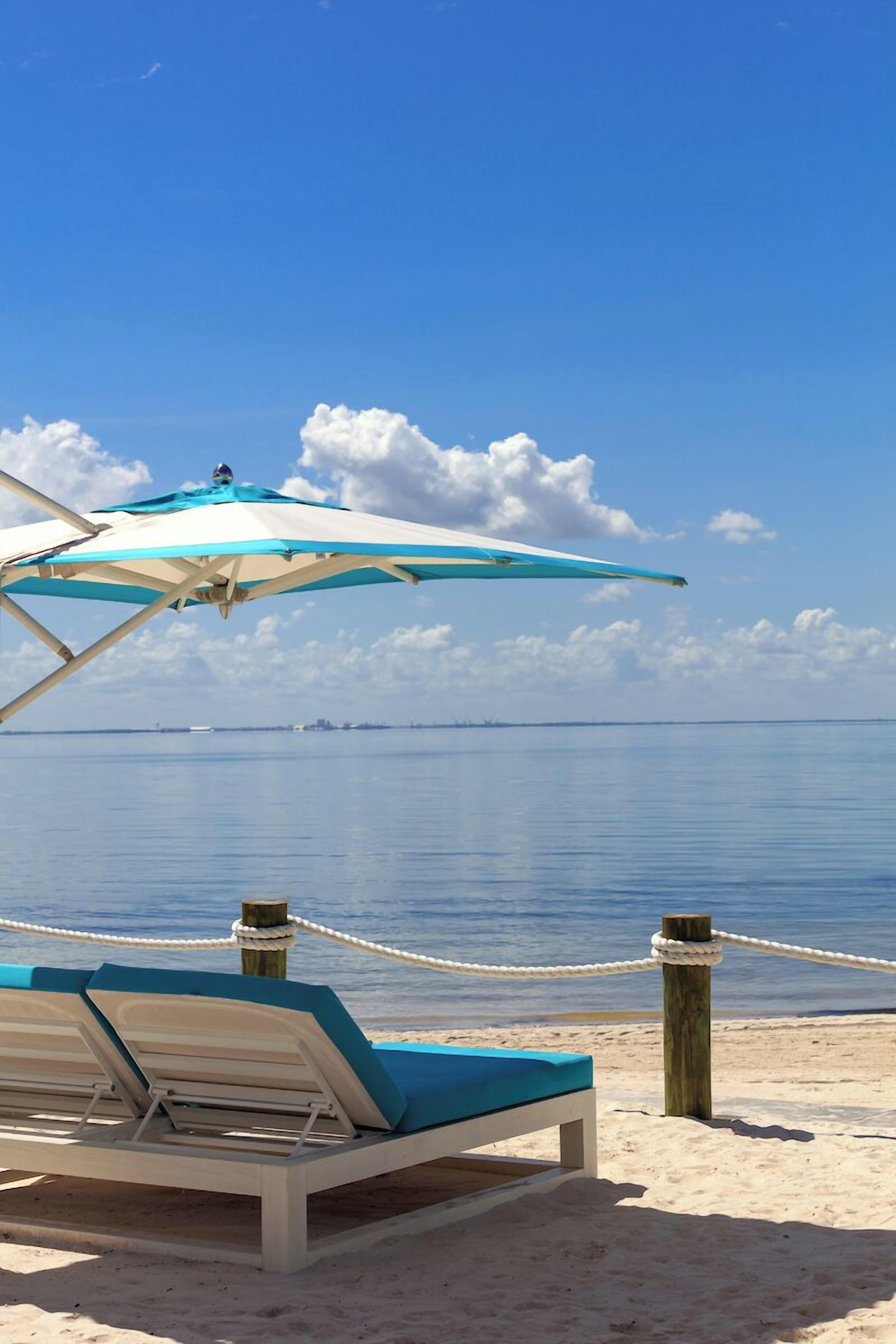 A beach with a lounge chair and a blue umbrella.