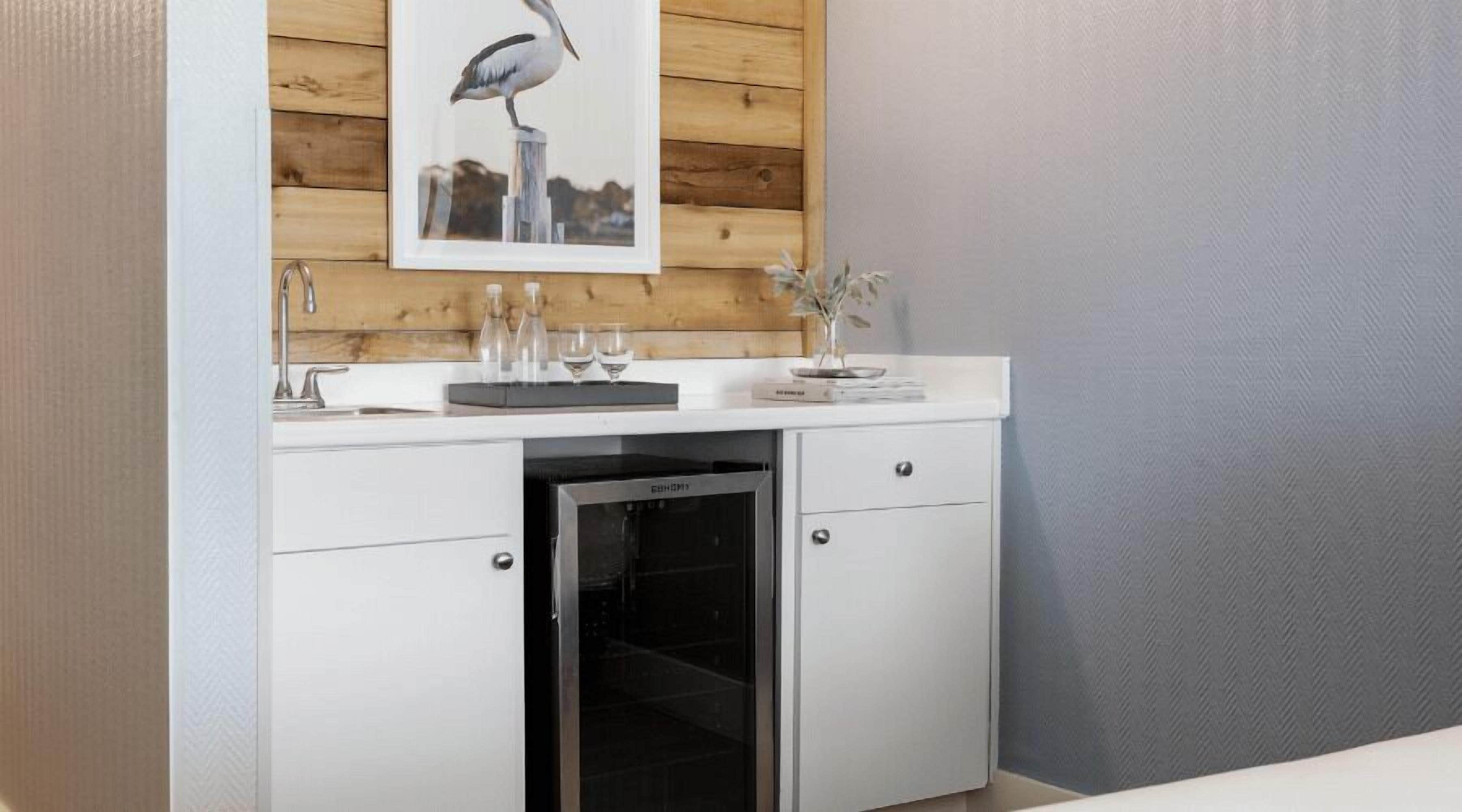 Una kitchenette equipada con horno empotrado, un lavamanos y una encimera con cristalería y un adorno.