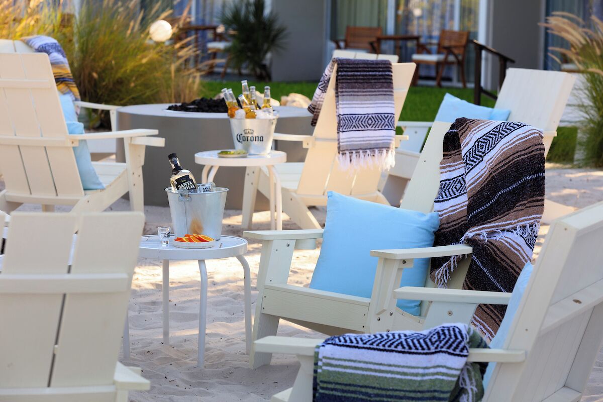 Outdoor seating with white chairs, a table with a bucket of Corona beer, and a blanket.