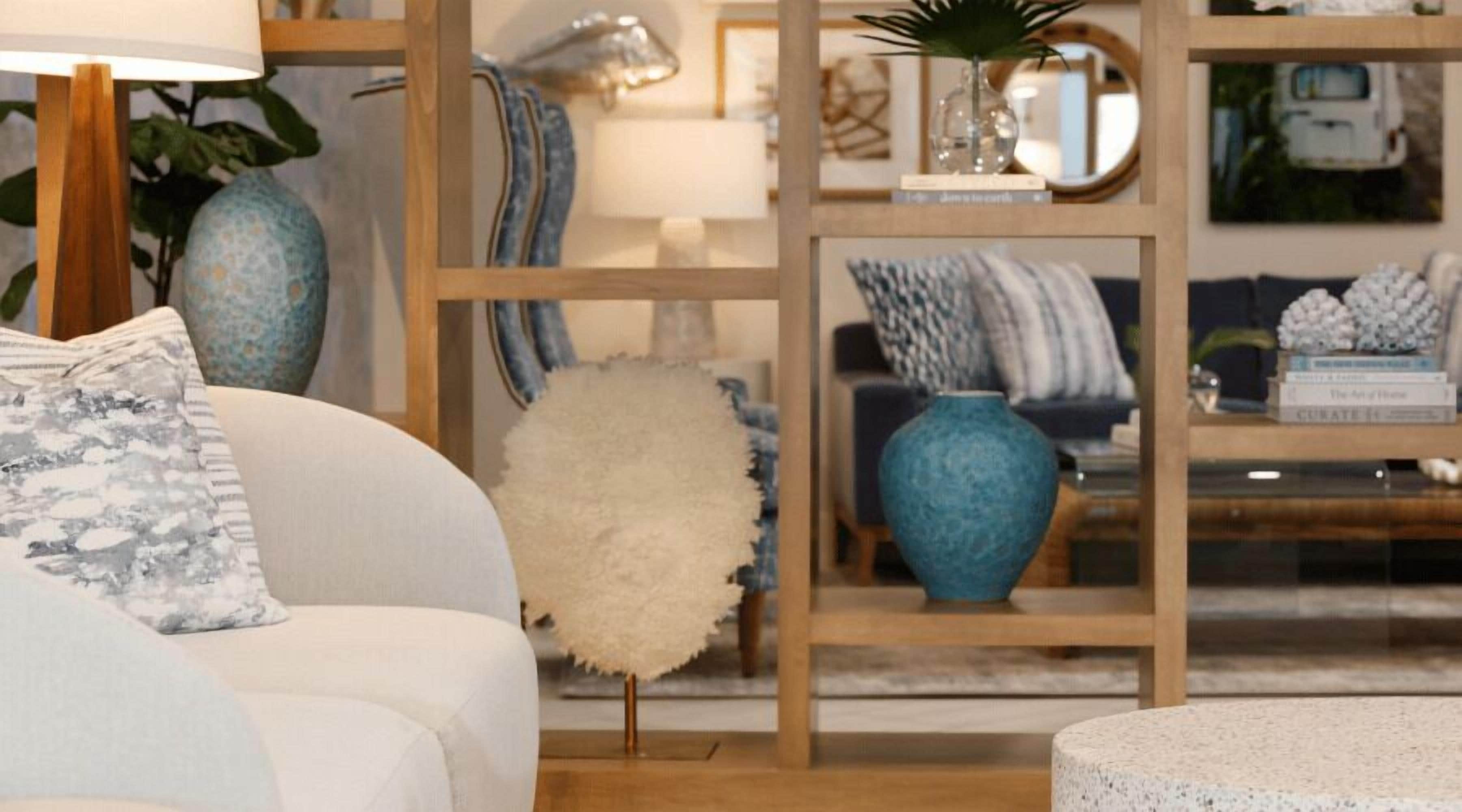 Una sala de estar moderna con un sofá blanco, un otoman blanco y mullido, y un jarrón azul sobre una estantería de madera.