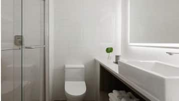 A modern bathroom with a glass shower enclosure, a toilet, and a white bathtub with a large mirror above it.