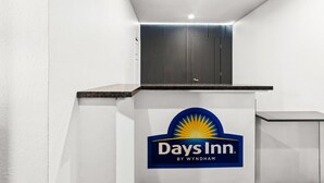 Een receptiebalie met het logo van Days Inn by Wyndham, een witte muur en een plafond met inbouwverlichting.