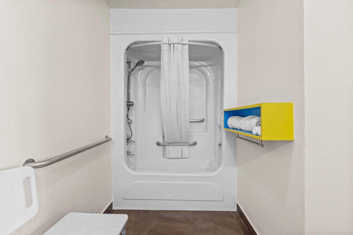 Une salle de bain avec une baignoire, des toilettes blanches, une barre d’appui et un porte-serviettes.