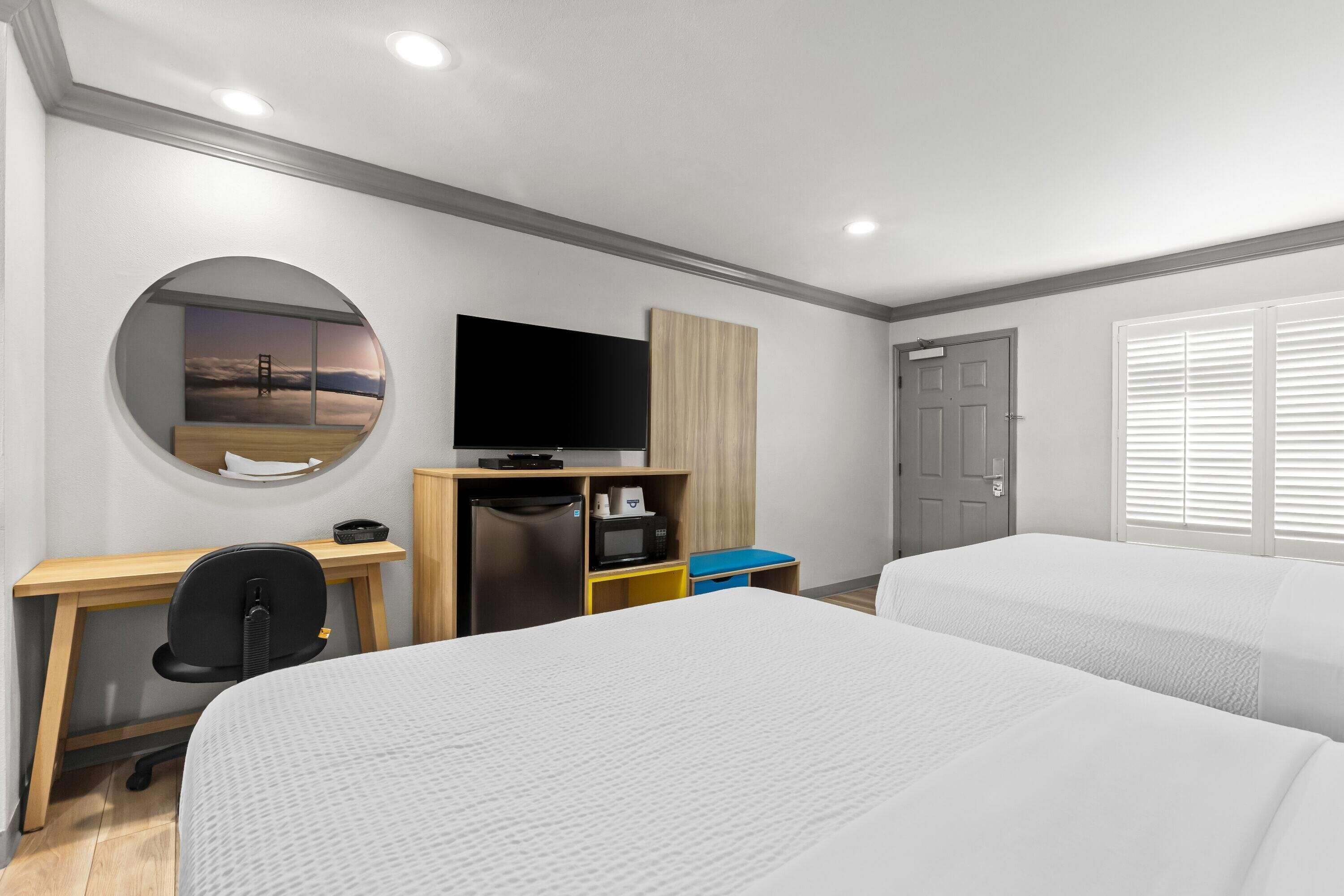 A hotel room with a bed, desk, television, and a view of the sky through a circular window.