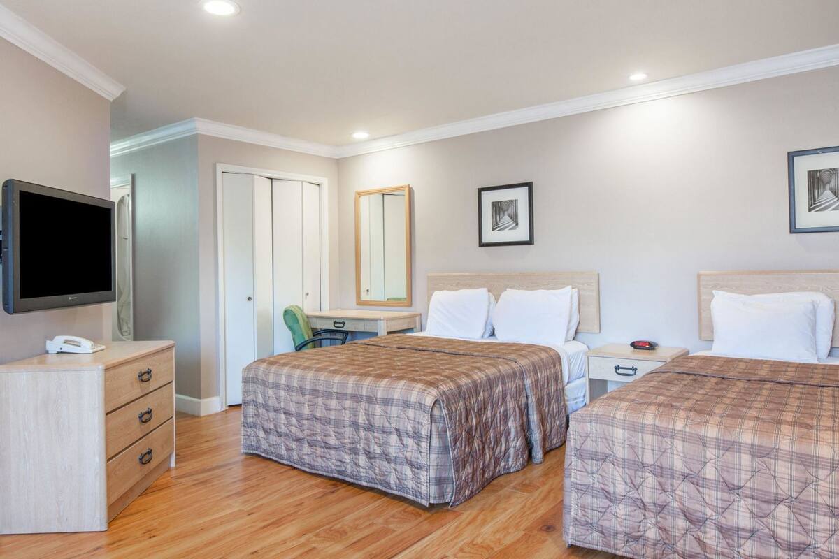 Une chambre d’hôtel avec deux lits, un bureau avec une chaise, une télévision et un miroir.