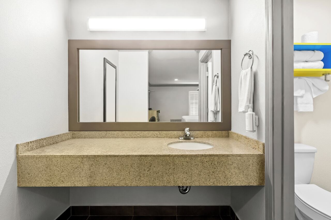 A bathroom with a granite countertop sink, a mirror, a towel rack, and a toilet.