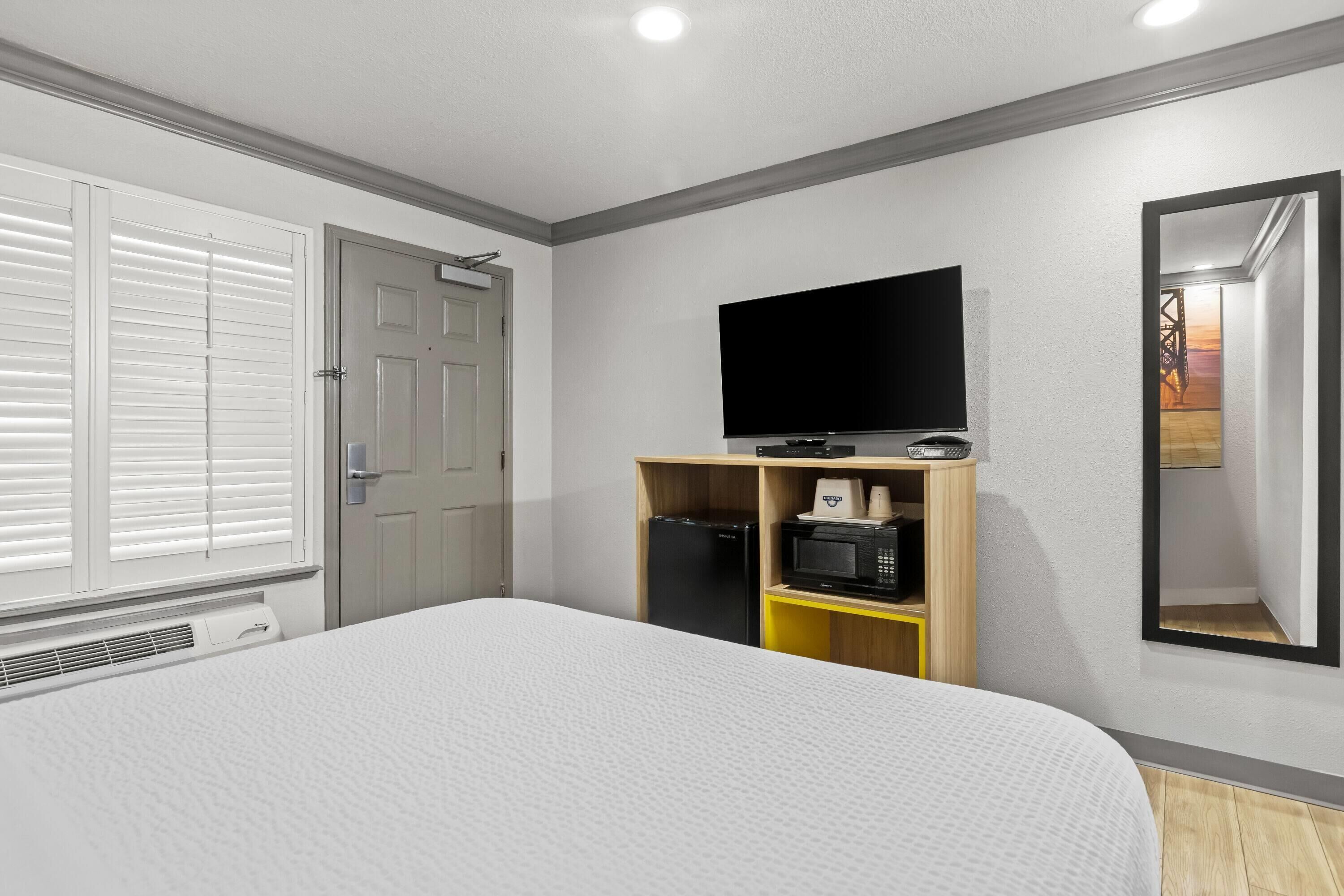 Un dormitorio con una cama, televisor, microondas y una puerta.